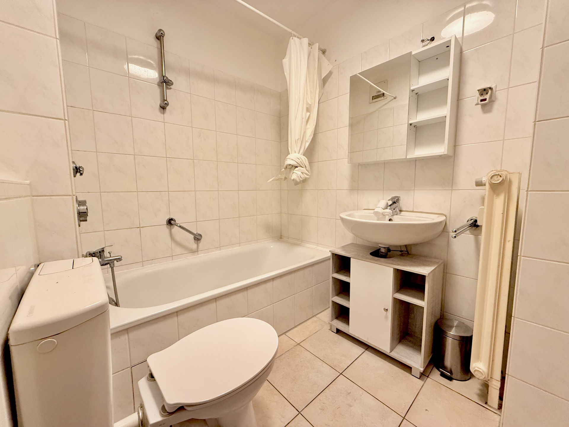 Kleines Badezimmer mit Badewanne, Toilette, Waschbecken und Spiegelschrank.