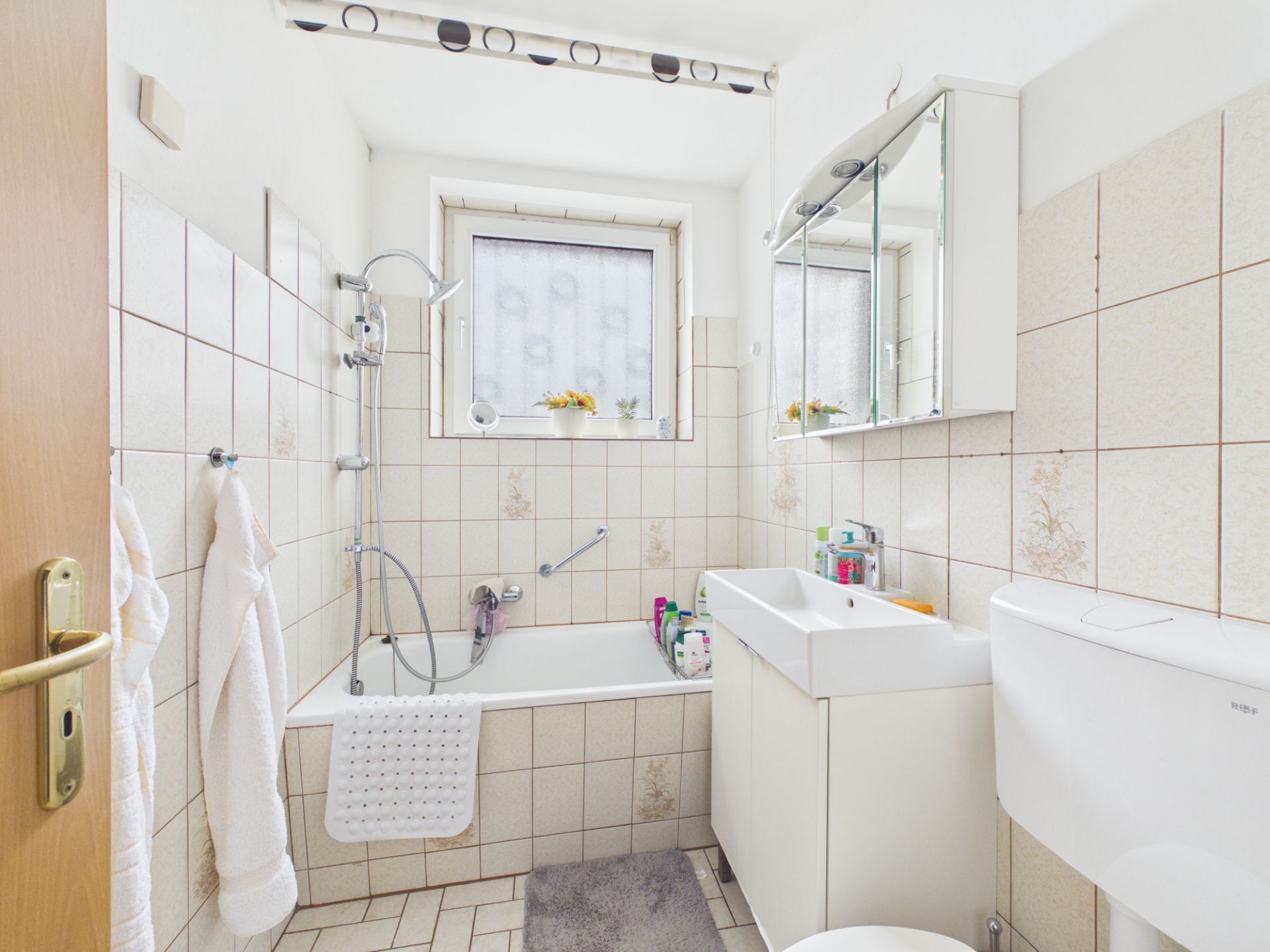 Helles Badezimmer mit Badewanne, Waschbecken, Spiegel, Toilette und Fenster.