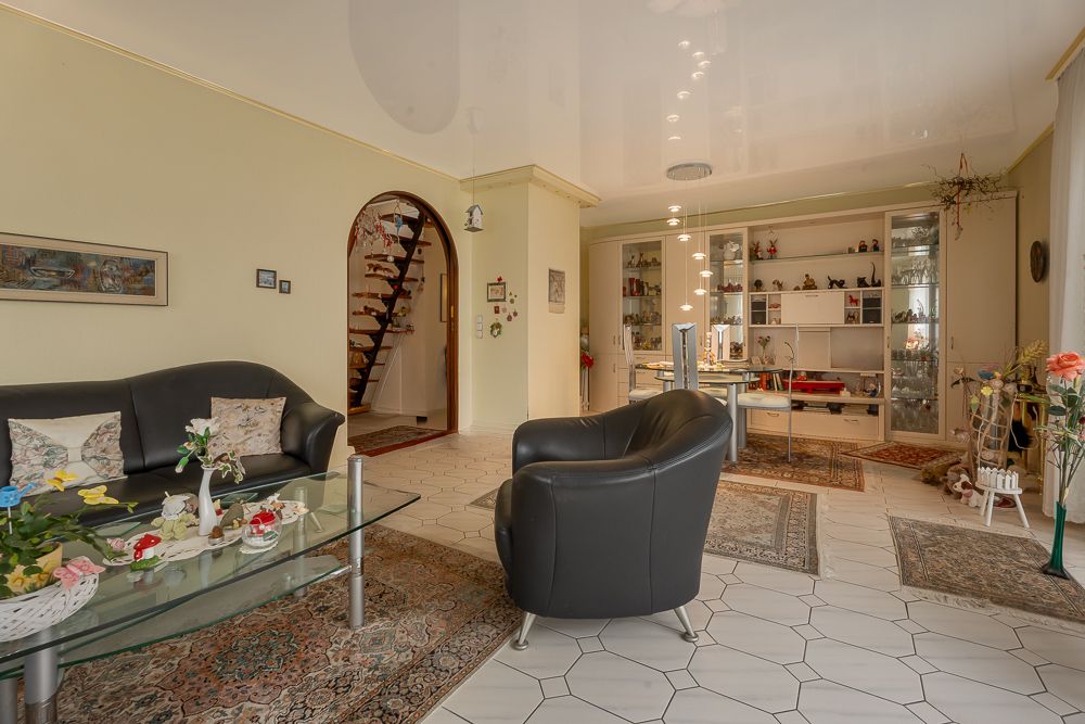 Helles Wohnzimmer mit Ledermöbeln, Glastisch, Teppichen und Regalwand im Hintergrund.