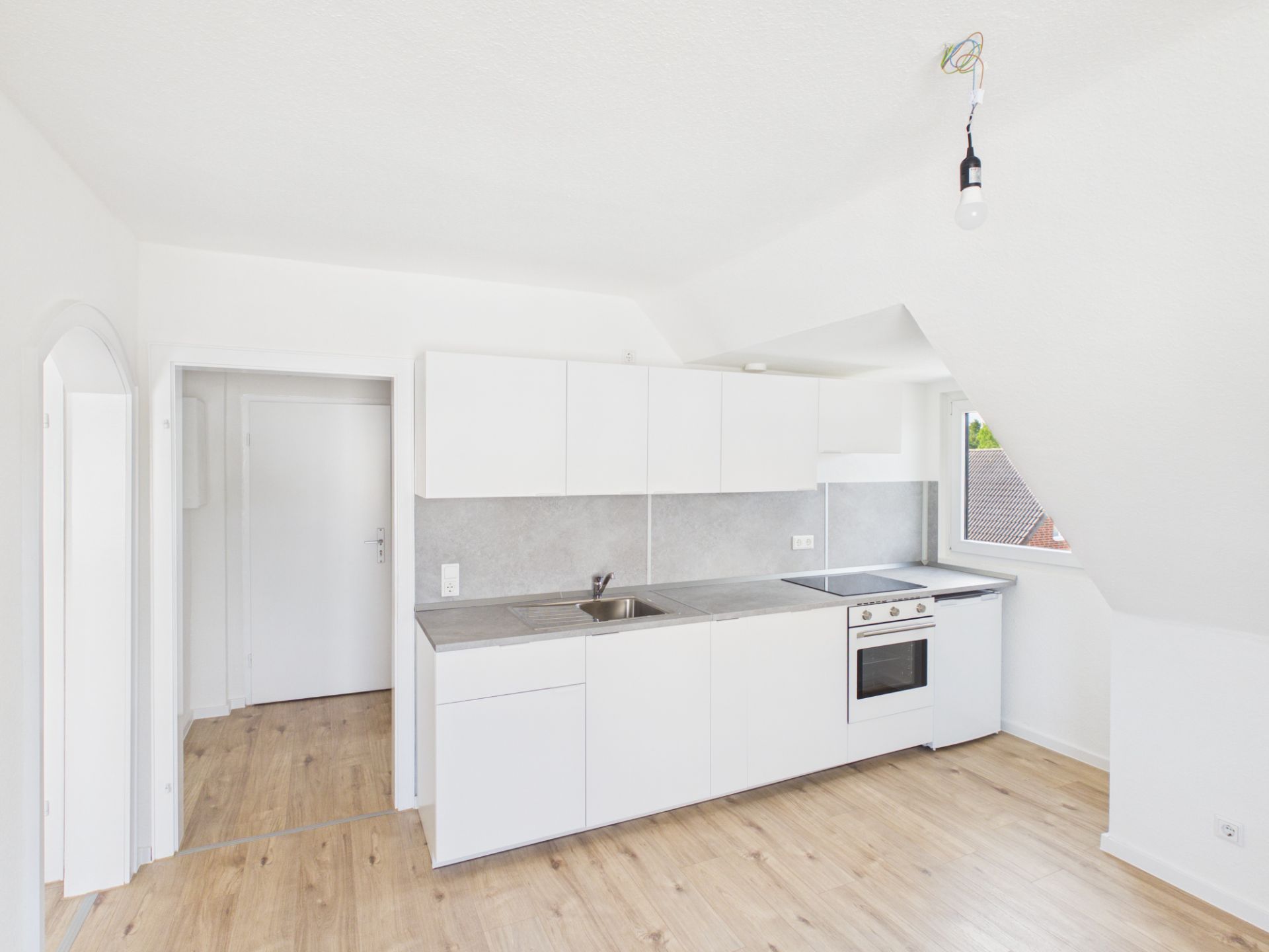 Helle Einbauküche mit weißen Schränken, Backofen, Spüle und Fenster, Holzboden.