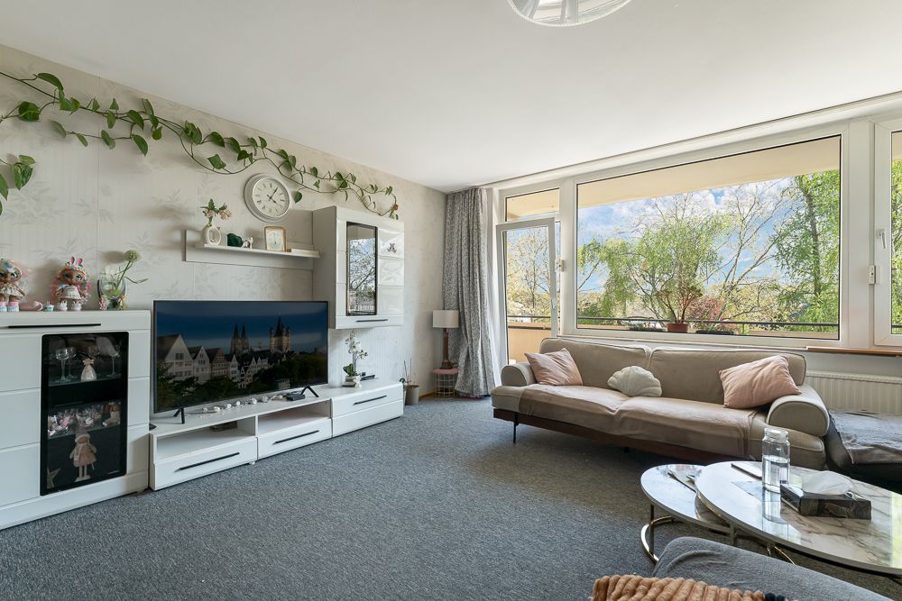 Helles Wohnzimmer mit Sofa, TV, Pflanzen und großem Fenster mit Blick nach draußen.