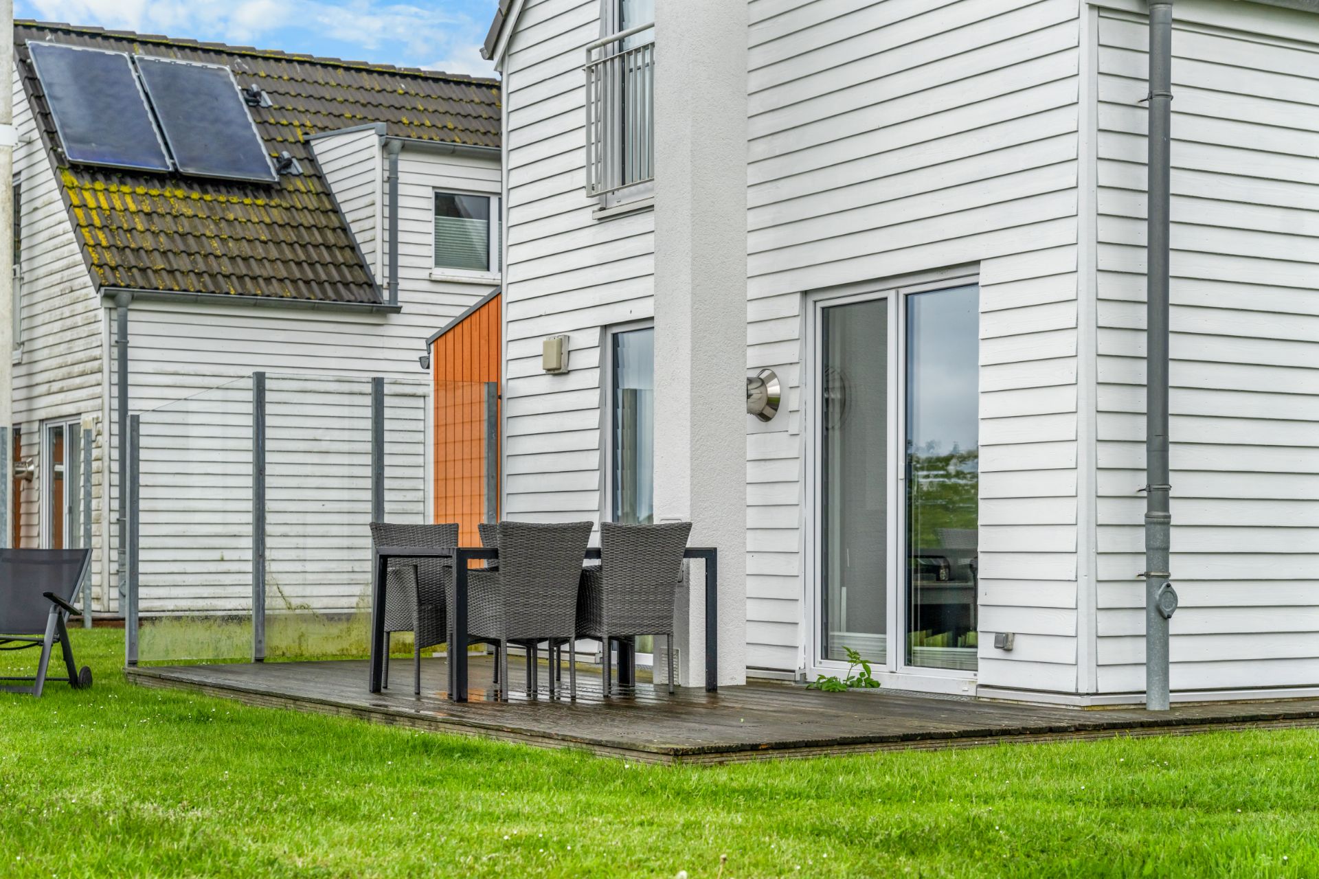 Weiße Hausfassade mit Terrasse, Gartentisch und vier Stühlen auf grünem Rasen.