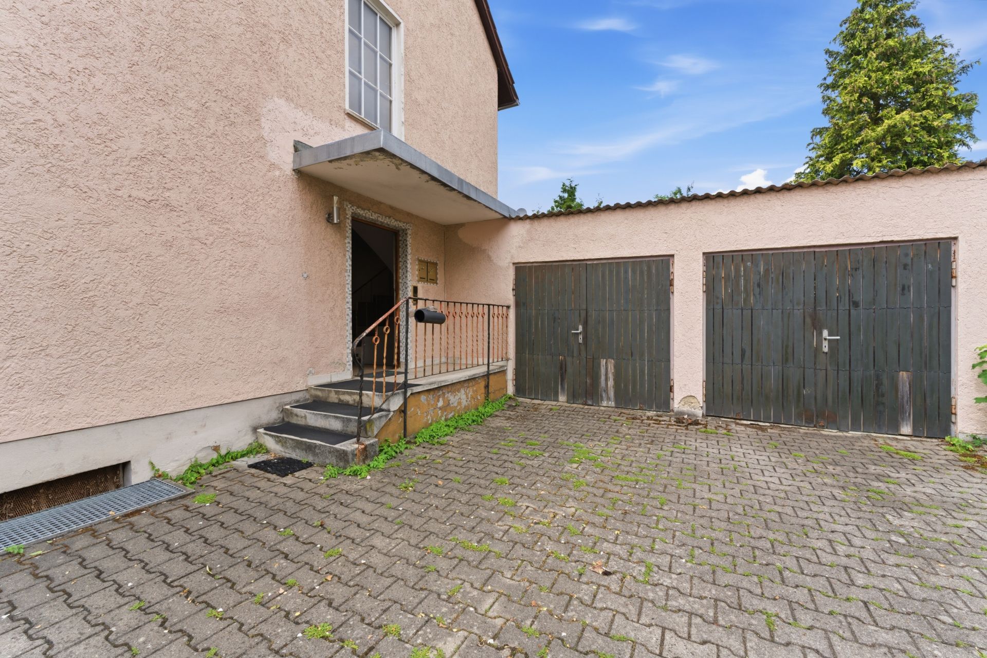 Eingangsbereich eines Hauses mit Treppe und zwei Garagentoren daneben.