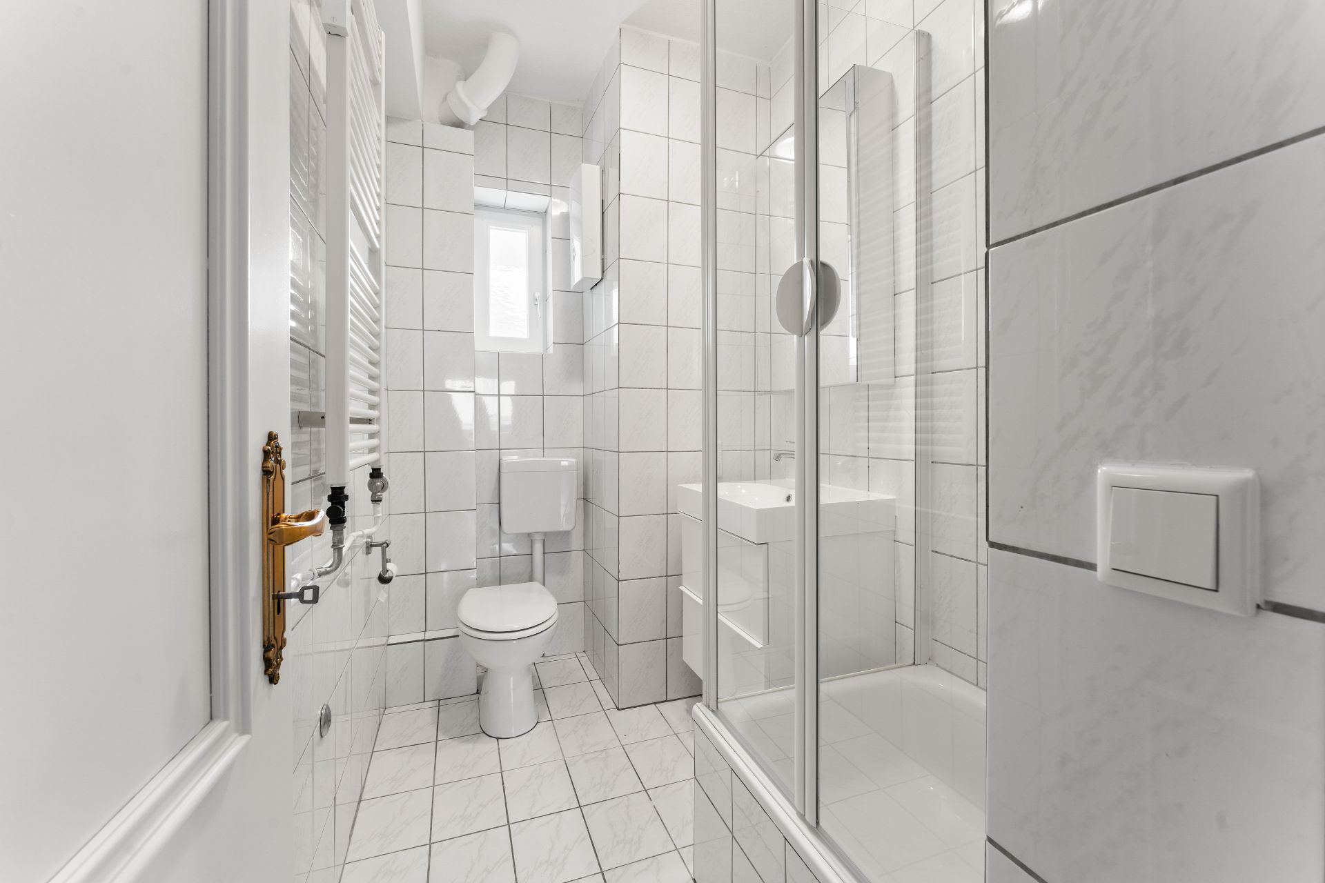 Helles Badezimmer mit Dusche, Toilette, Waschbecken und Fenster, alles gefliest.