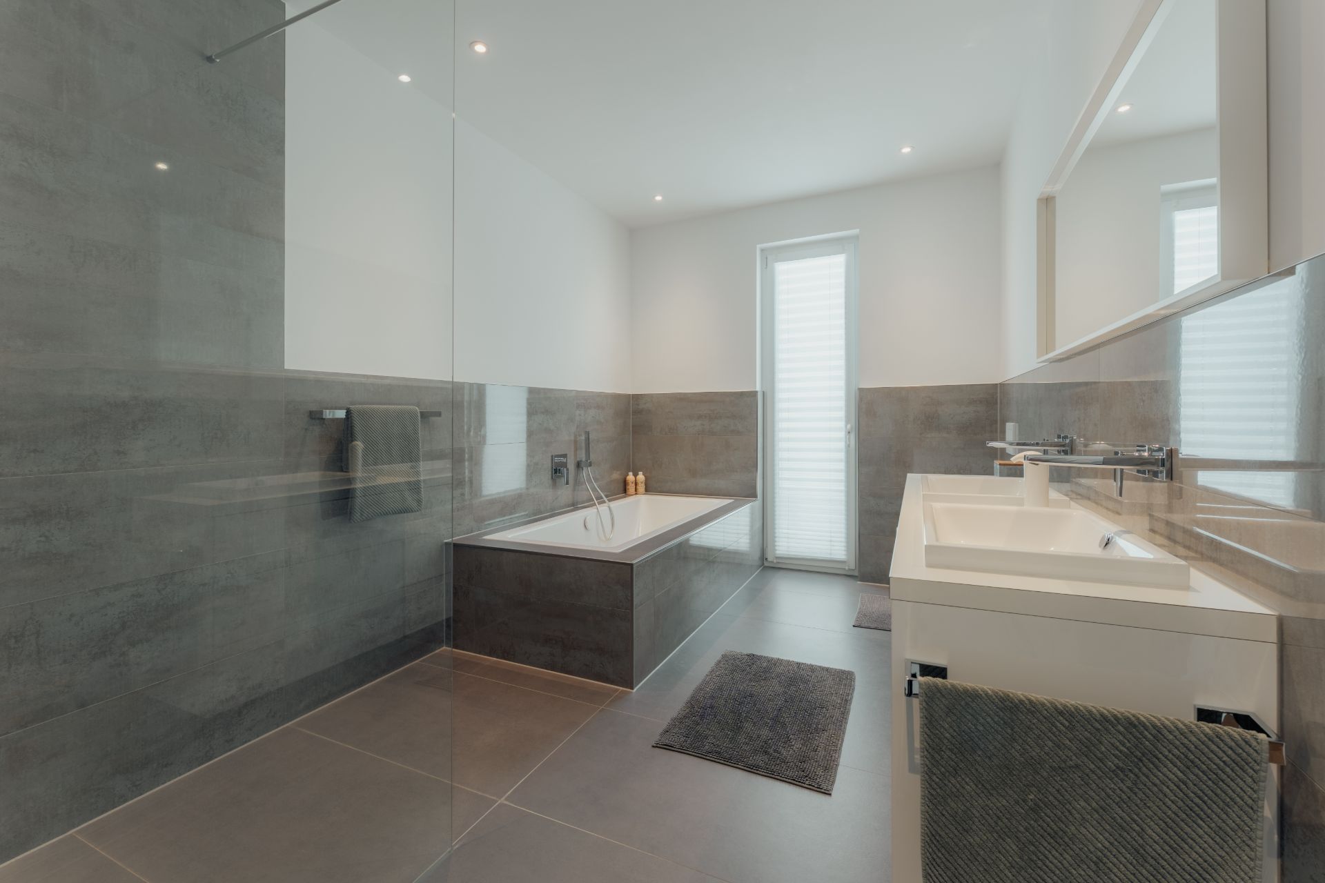 Modernes Badezimmer mit Badewanne, Doppelwaschbecken, großem Spiegel und grauen Fliesen.