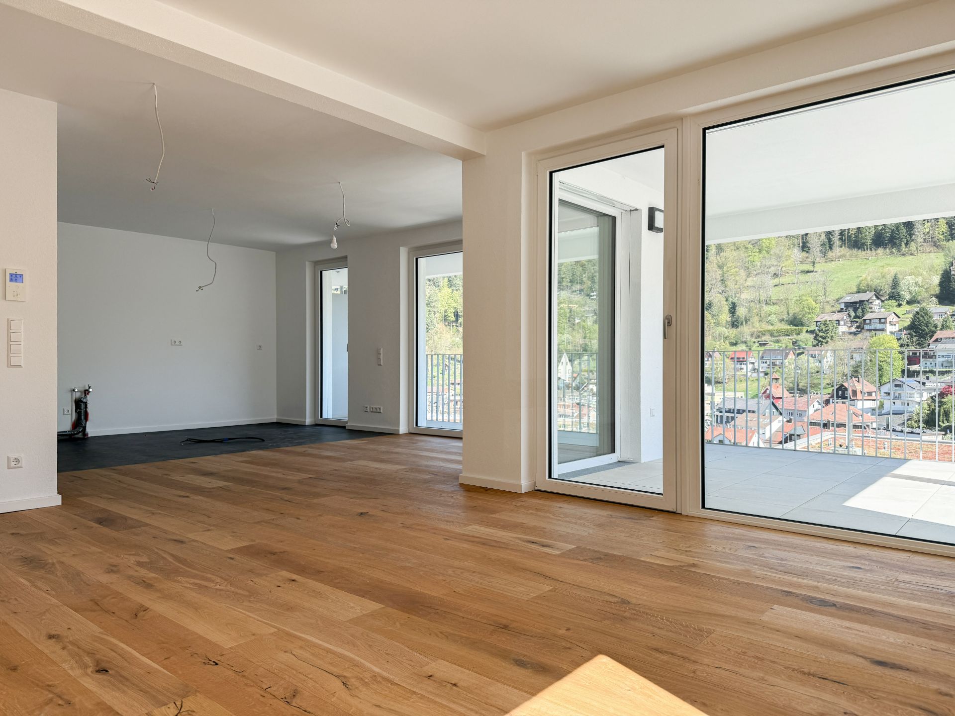 Helles Wohnzimmer mit Holzboden, großen Fenstern und Zugang zu einem Balkon mit Aussicht.