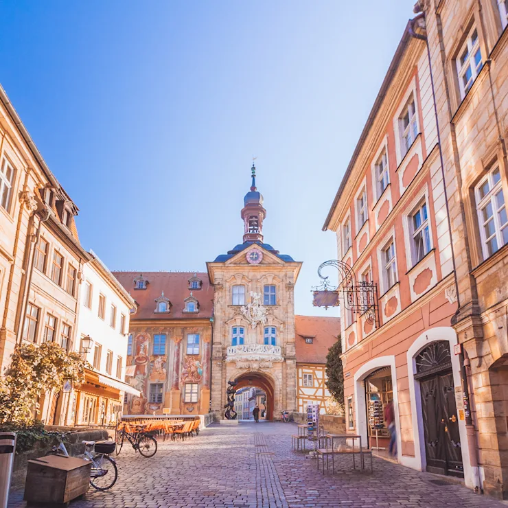 Historisches Gebäude mit bemalter Fassade und Turm, umgeben von alten Häusern und Kopfsteinpflaster.
