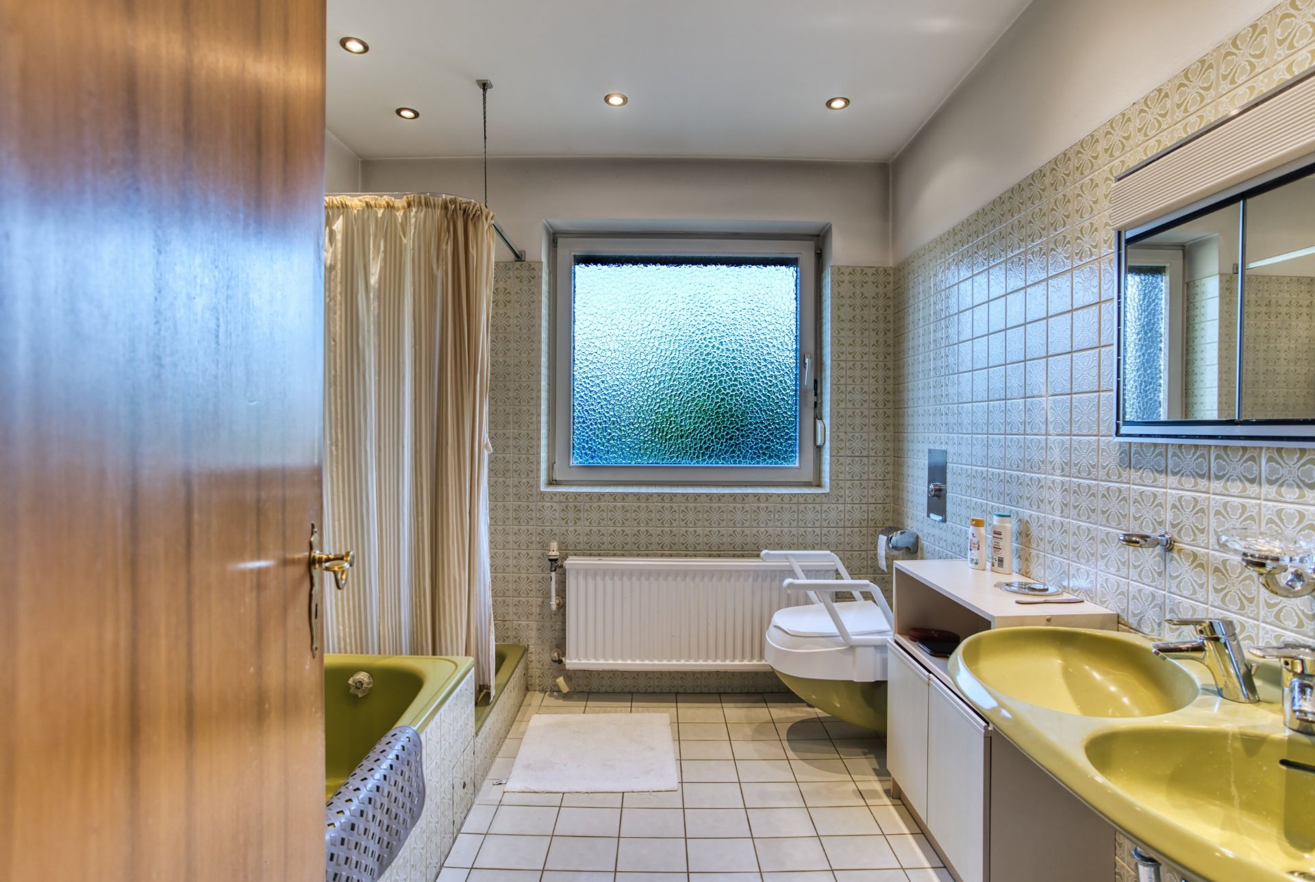 Badezimmer mit gelbem Waschbecken, Badewanne, WC mit Haltegriff und Fenster mit Sichtschutzglas.