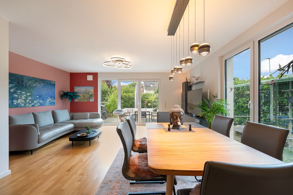 Helles Wohnzimmer mit Esstisch, Sofa, Pflanzen und großen Fenstern zum Garten.