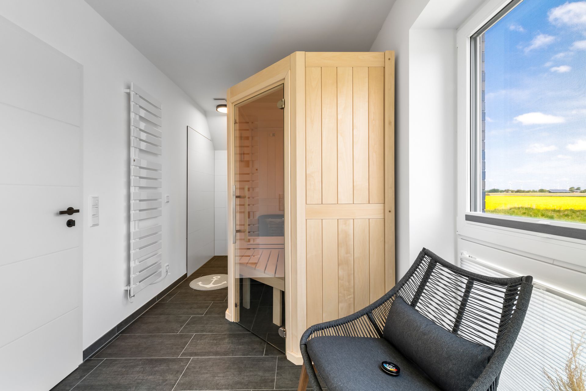 Heller Flur mit Sauna, Stuhl am Fenster und weißem Handtuchheizkörper an der Wand.