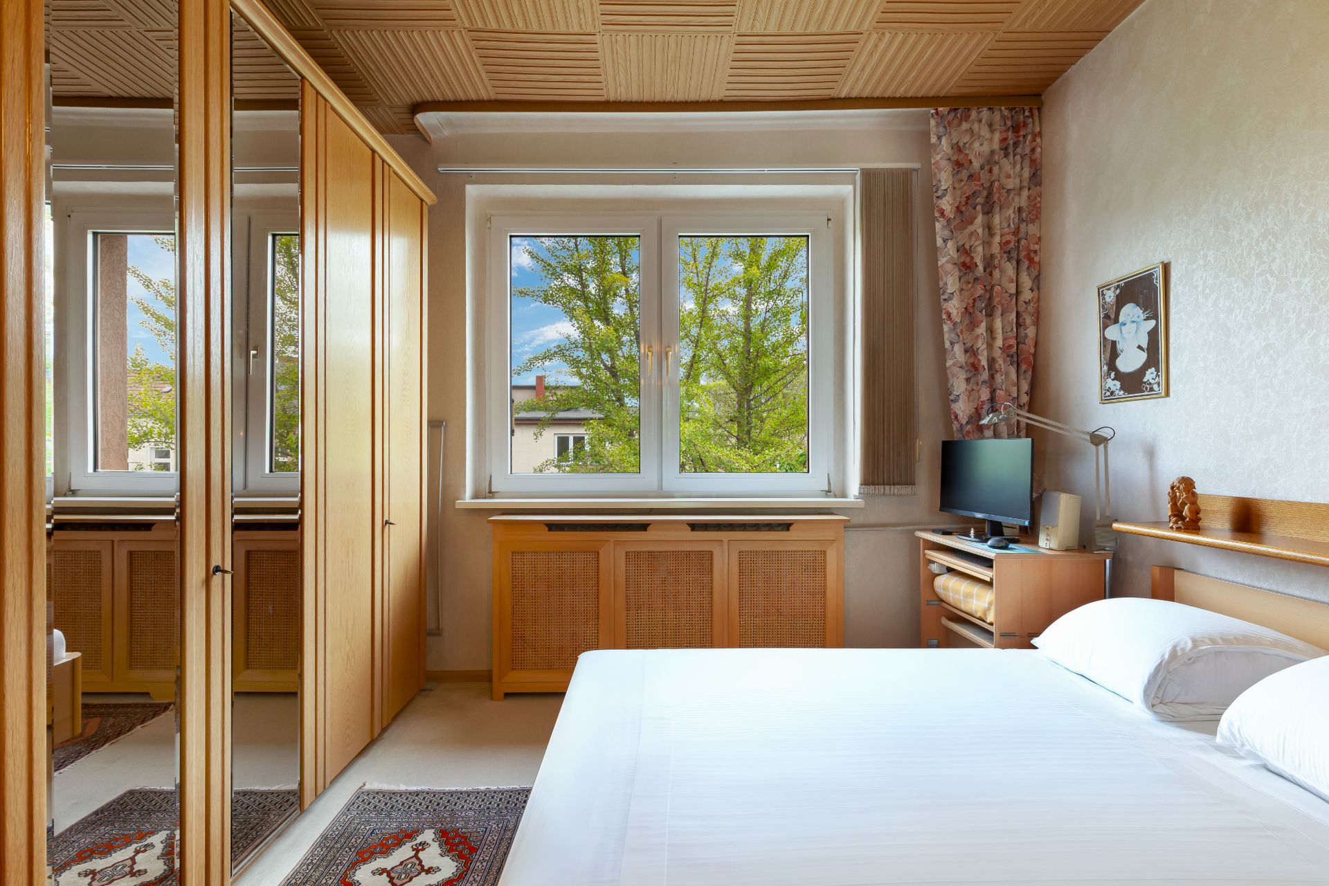 Schlafzimmer mit großem Fenster, Doppelbett, Kleiderschrank mit Spiegeln und kleinem Schreibtisch.