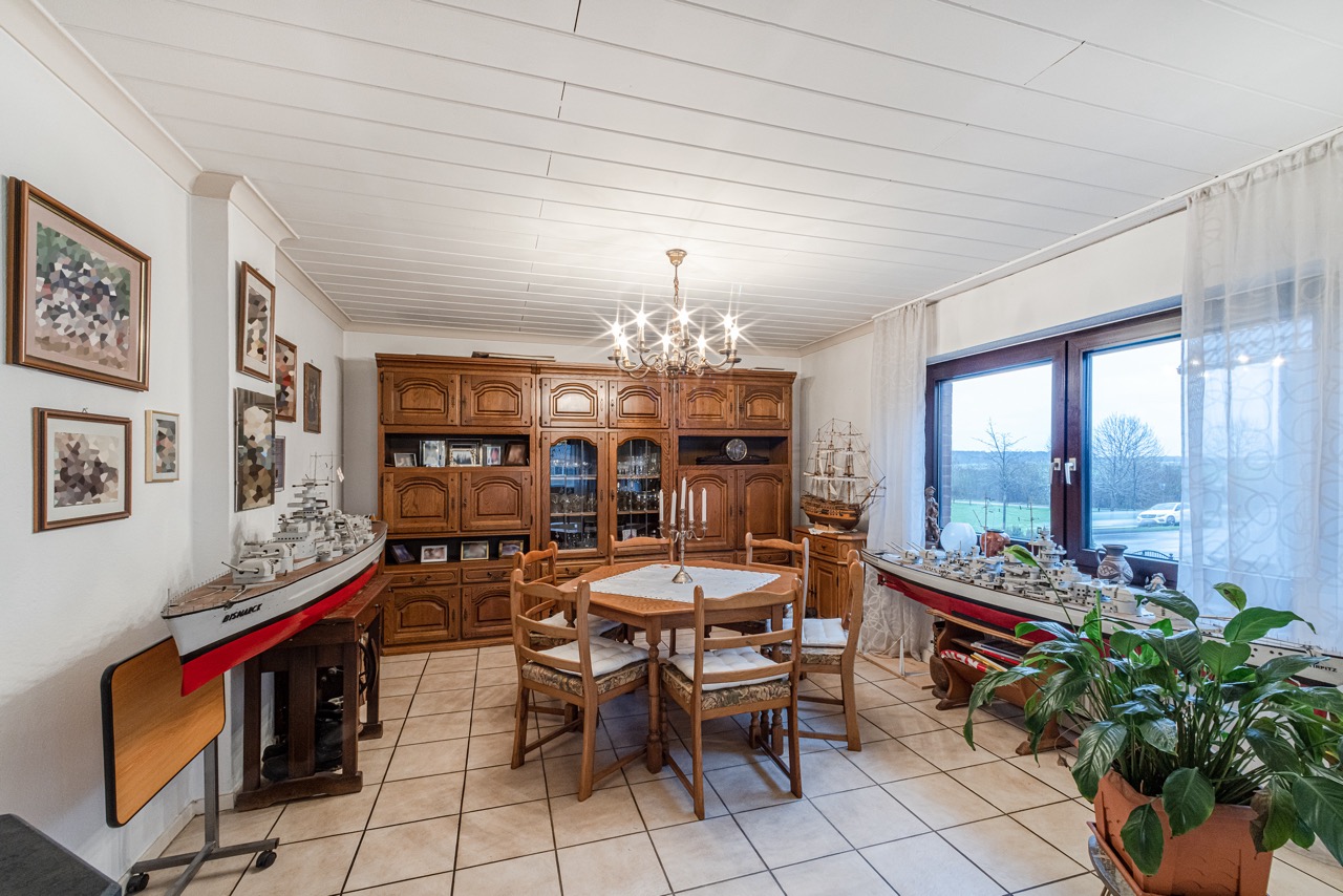 Esszimmer mit Holzmöbeln, großem Fenster, Schiffsmodellen und Bildern an der Wand.
