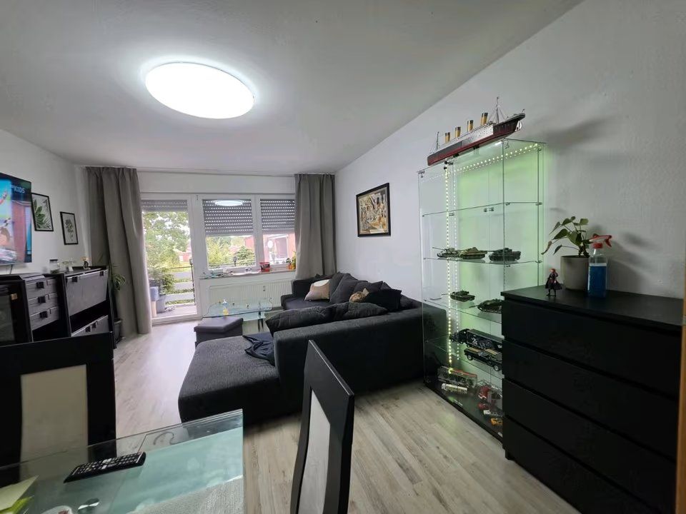 Wohnzimmer mit grauem Sofa, Vitrine, Kommode, Esstisch und großem Fenster mit Vorhängen.