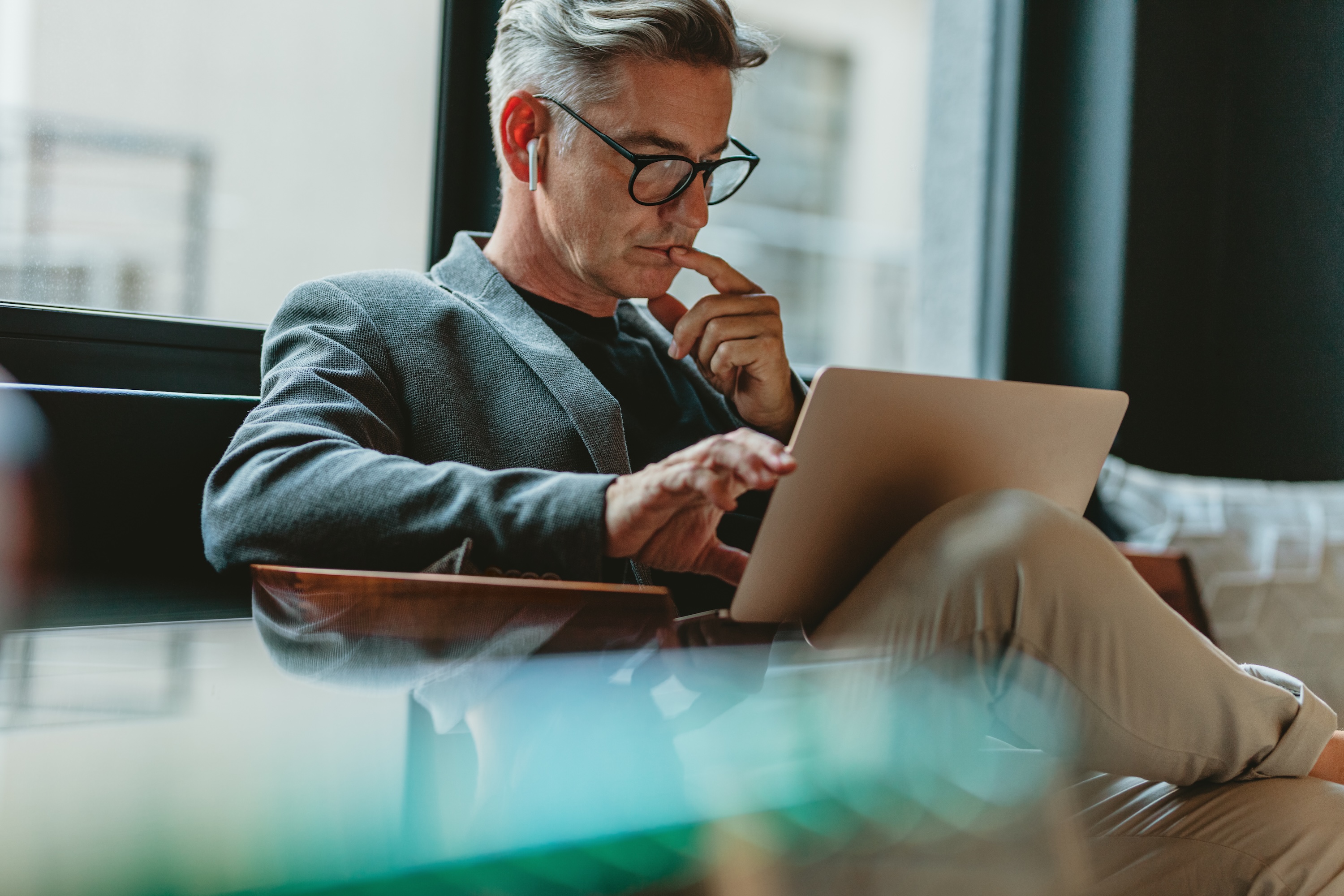Ein Mann mit Brille sitzt auf einem Stuhl und arbeitet an einem Laptop.