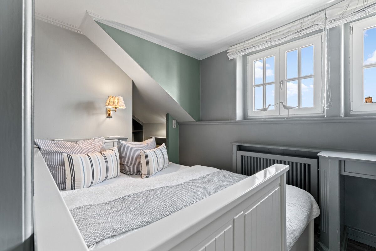 Helles Schlafzimmer mit Doppelbett, gestreiften Kissen und Fenster mit Blick nach draußen.