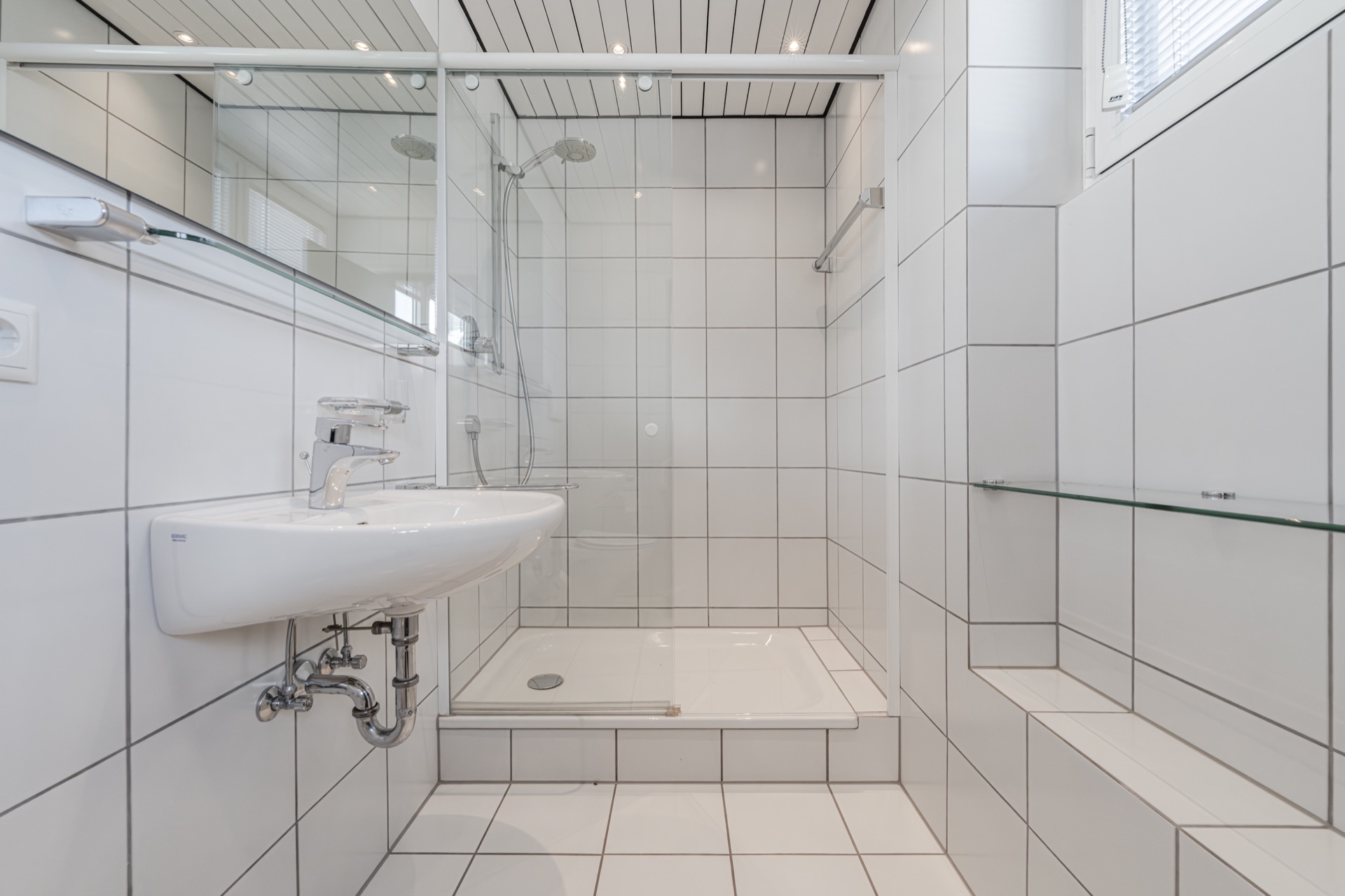 Helles Badezimmer mit Dusche, Waschbecken und gefliestem Boden.