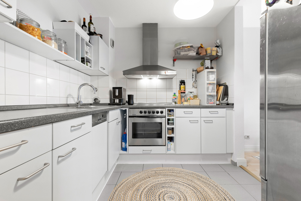 Moderne Küche mit weißen Schränken, Herd, Spüle und Edelstahlkühlschrank.