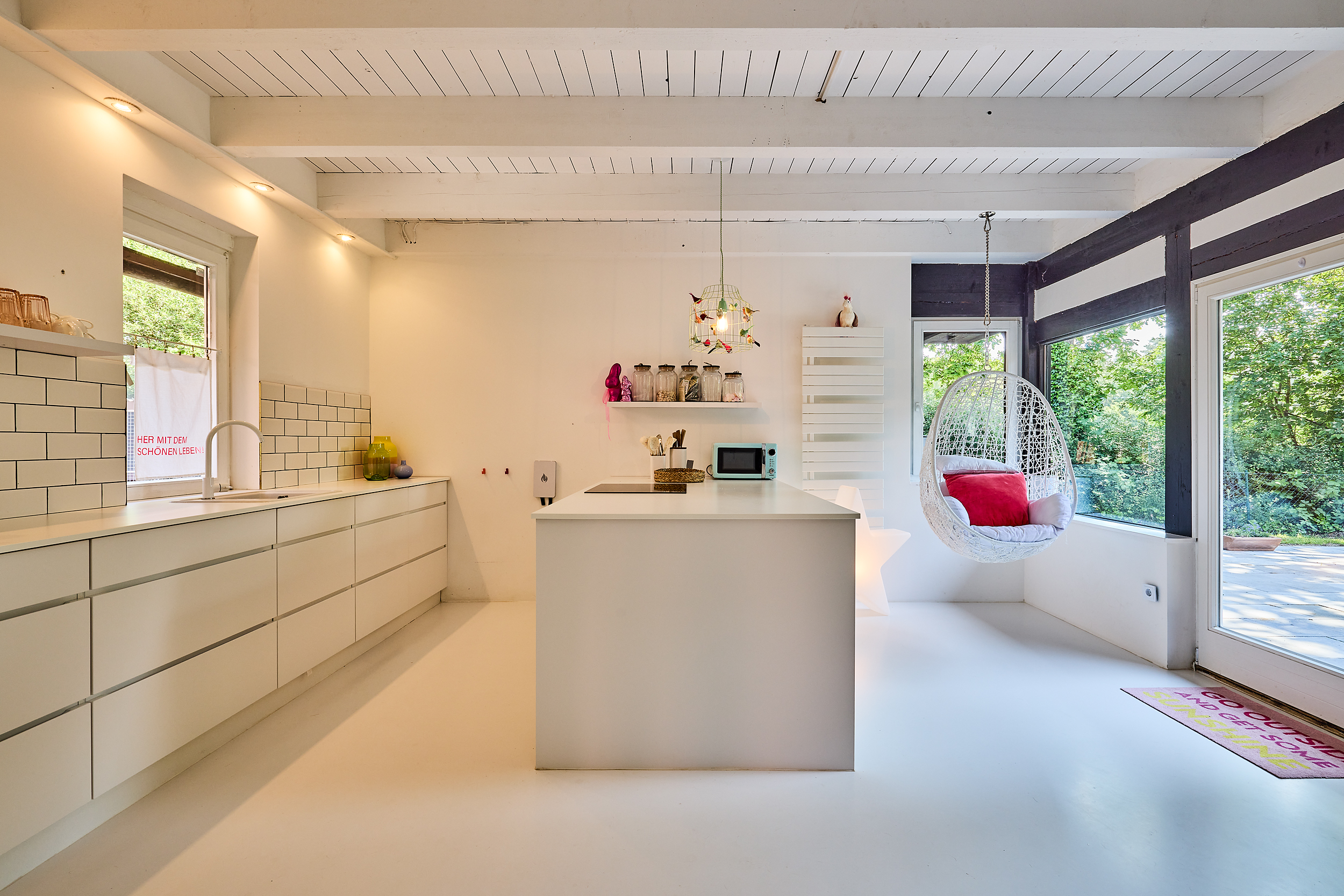 Moderne, helle Küche mit Kochinsel, Hängesessel und großen Fenstern mit Blick ins Grüne.