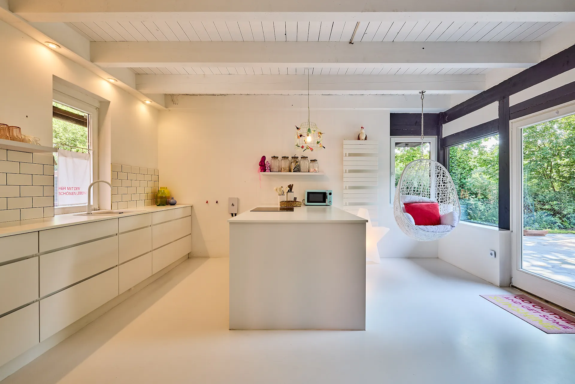 Moderne, helle Küche mit Kochinsel, Hängesessel und großen Fenstern mit Blick ins Grüne.