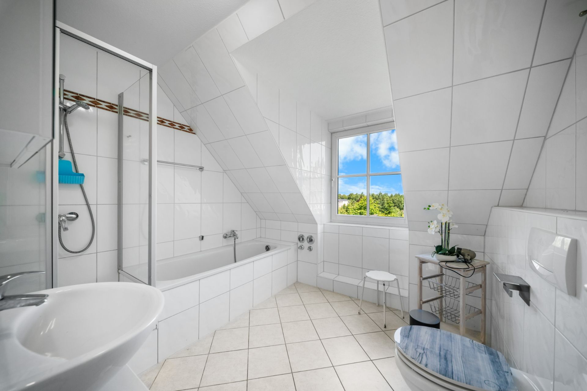 Helles Badezimmer mit Badewanne, Dusche, WC, Waschbecken und Fenster unter einer Schräge.