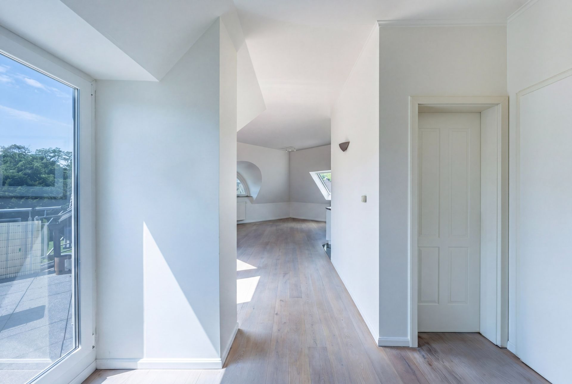 Heller Flur mit Holzboden, weißen Wänden und Zugang zu einem Balkon.