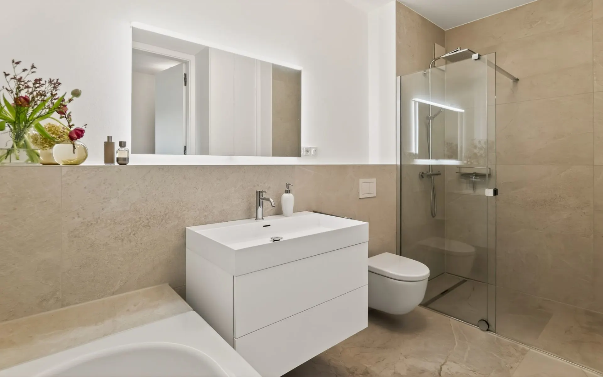 Modernes Badezimmer mit Glasdusche, weißem Waschbecken, WC und großem Spiegel.
