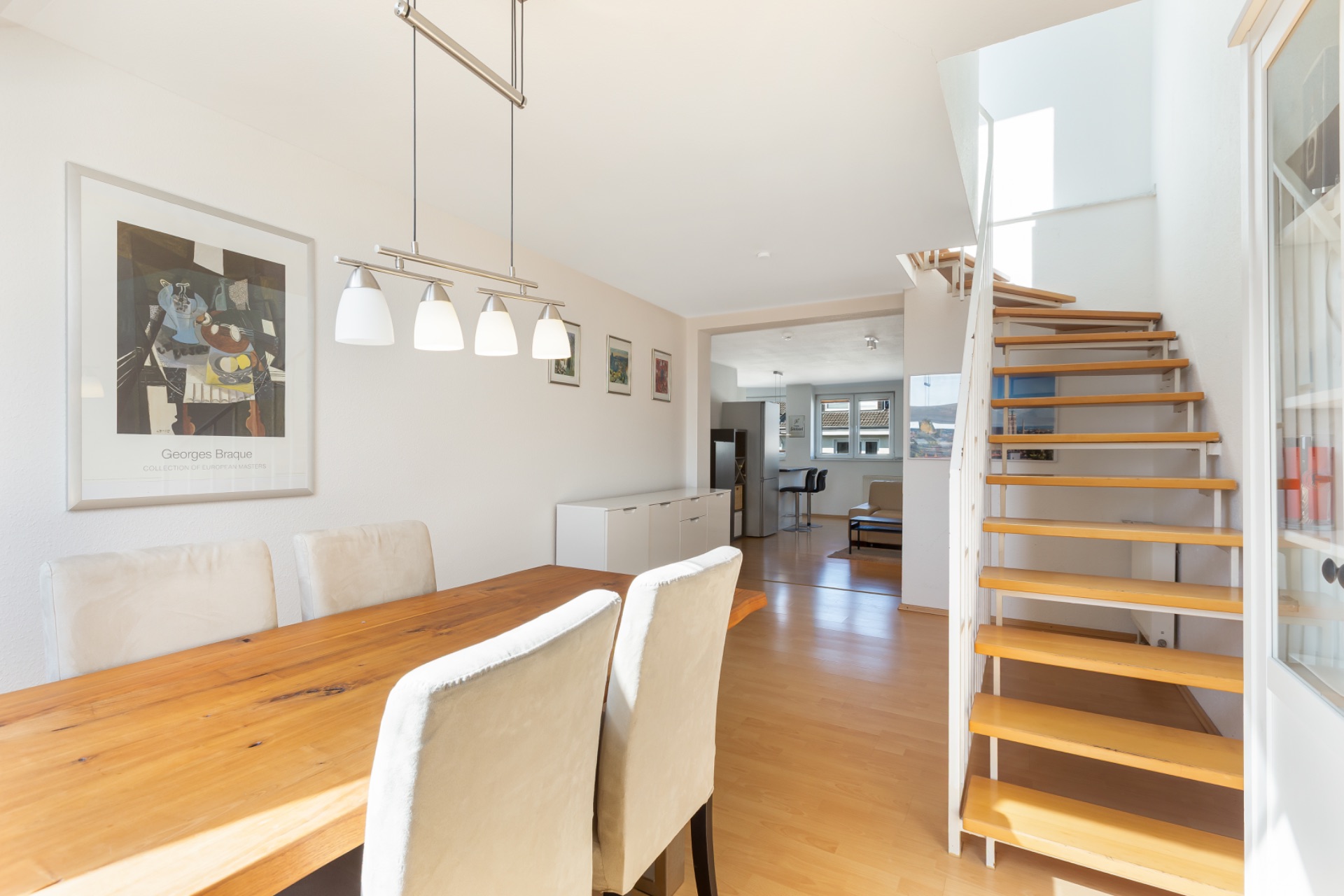 Helles Esszimmer mit Holztisch, gepolsterten Stühlen und Treppe aus Holz.