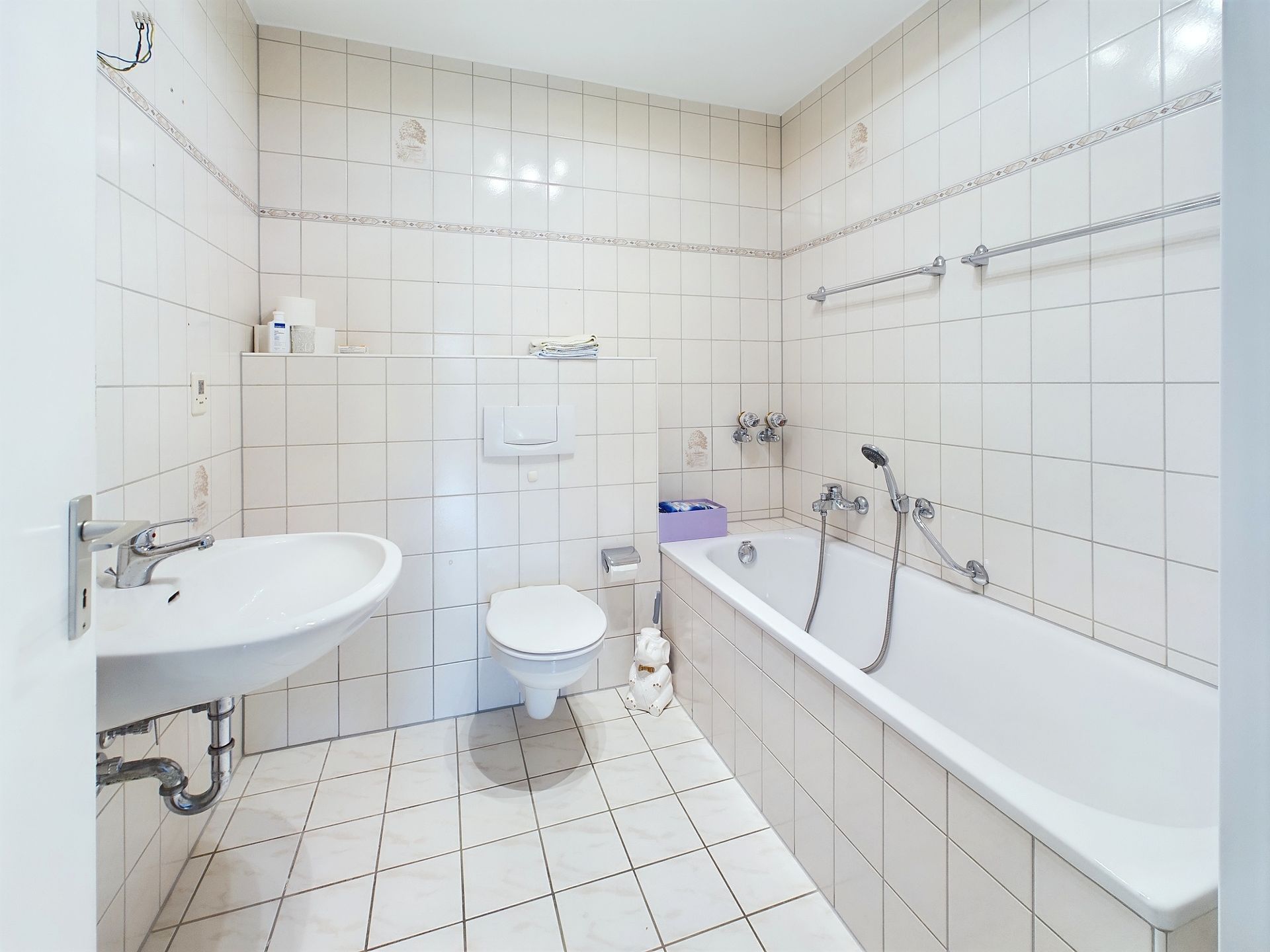 Helles Badezimmer mit Badewanne, Waschbecken und Toilette, weiße Fliesen an Wand und Boden.