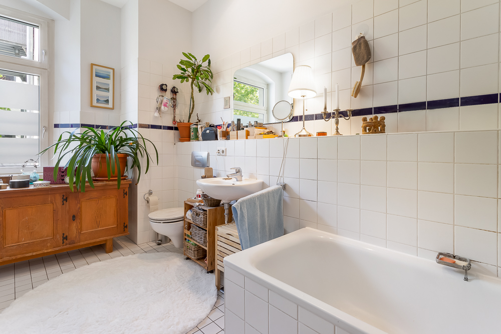Helles Badezimmer mit Badewanne, Waschbecken, WC, Pflanzen und Holzschrank.