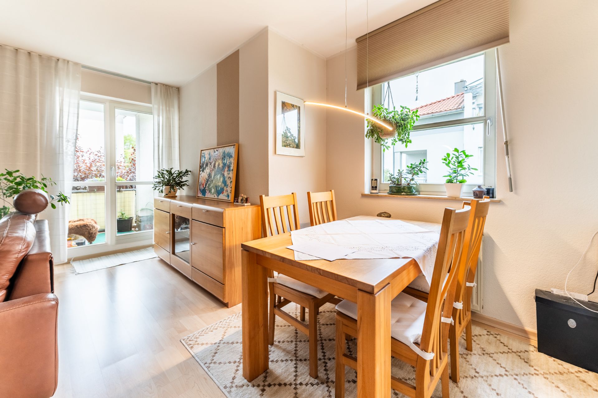 Essbereich mit Holztisch und vier Stühlen, Fenster, Pflanzen und Zugang zum Balkon.