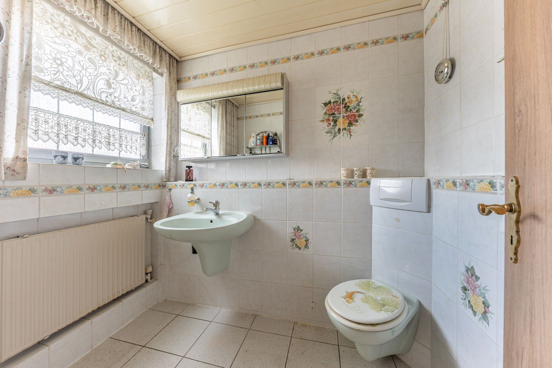 Helles Bad mit Waschbecken, Toilette, Spiegel und floralen Fliesenmotiven.
