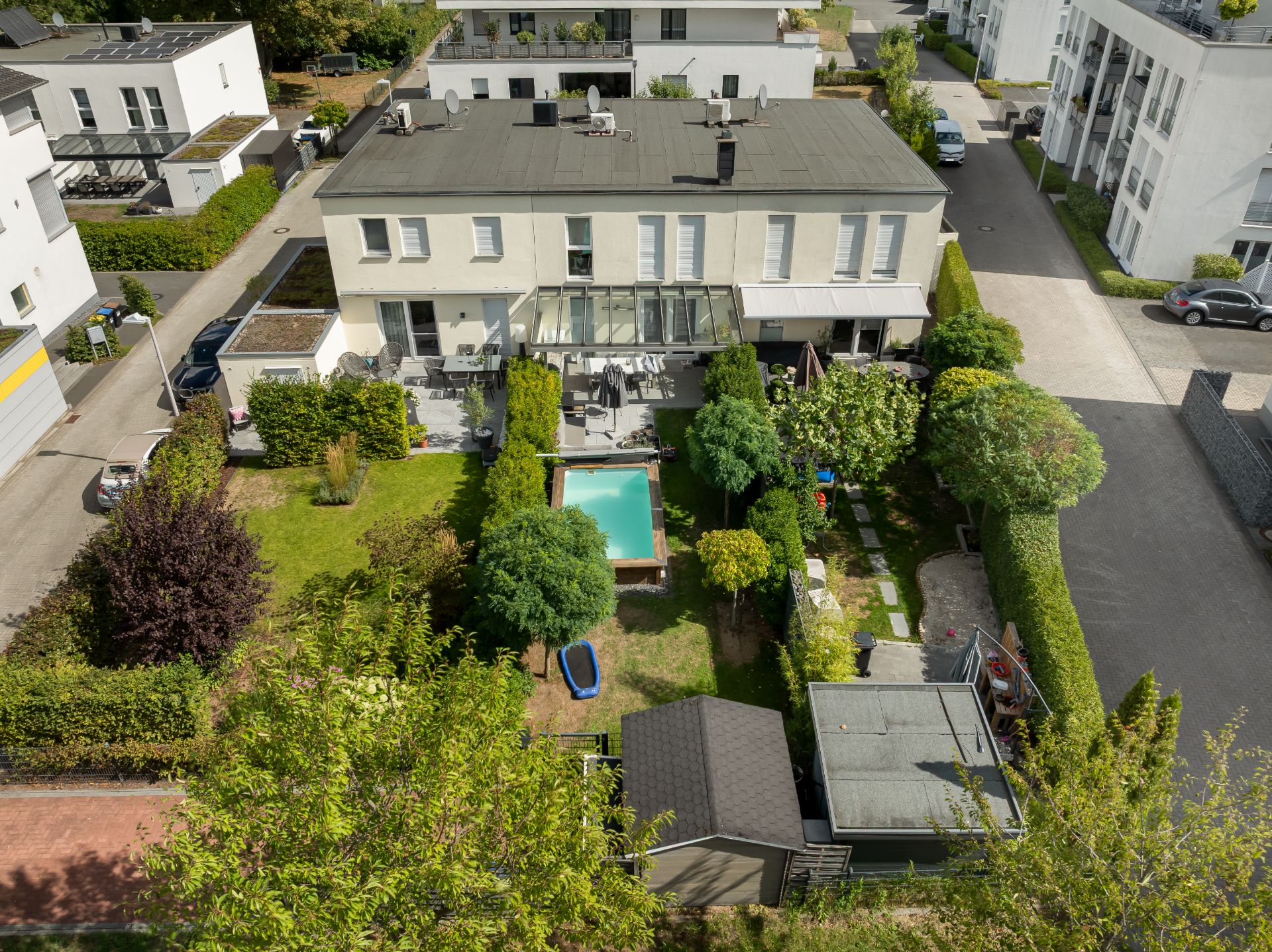 Luftaufnahme eines Gartens mit Pool und Terrasse hinter einem modernen Wohnhaus.
