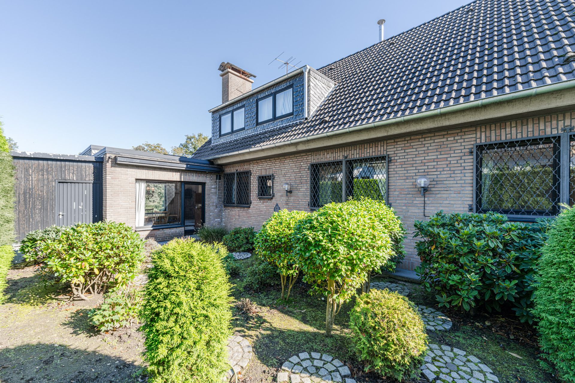 Vorderansicht eines Hauses mit Ziegelmauerwerk, Satteldach und gepflegtem Garten.
