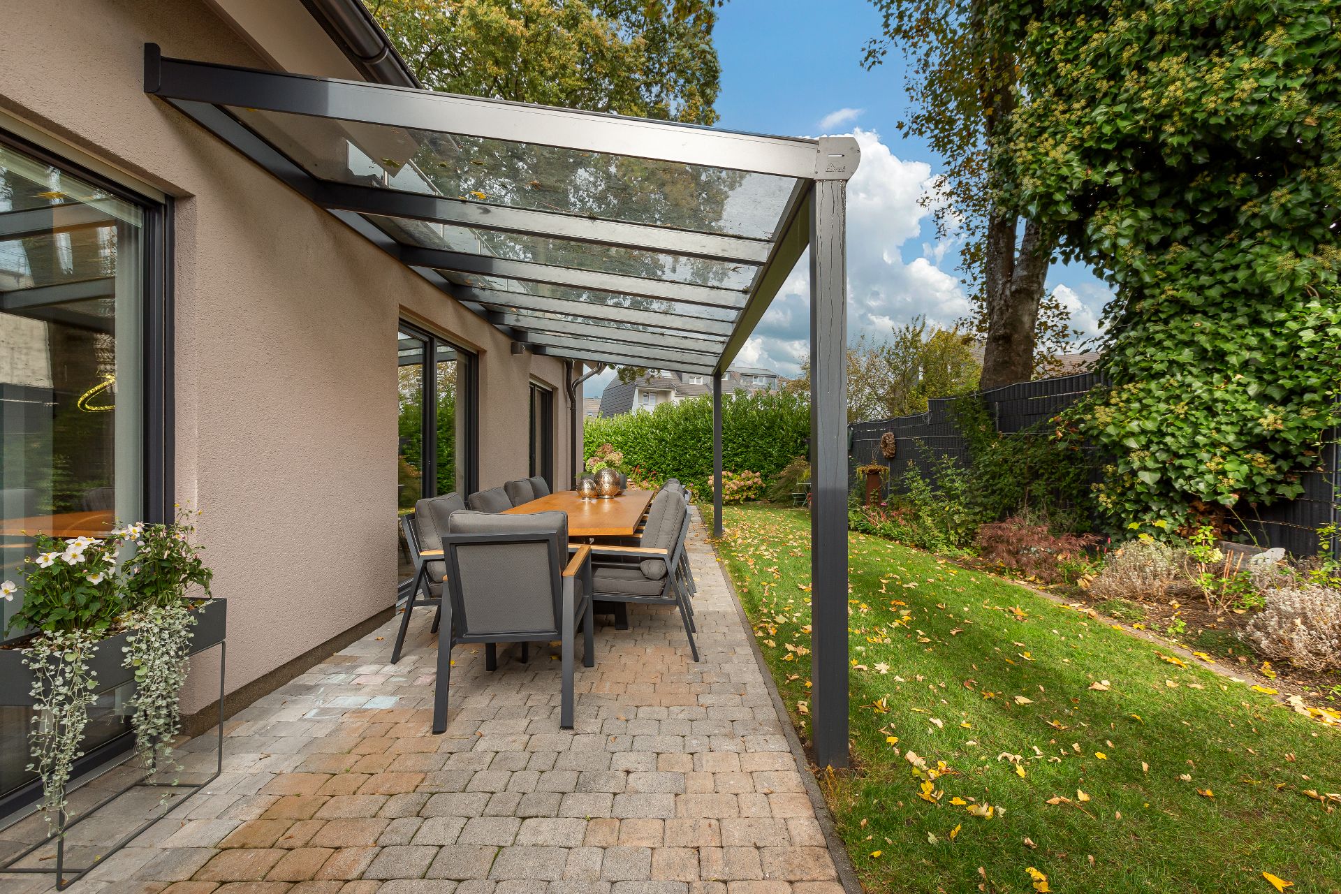 Überdachte Terrasse mit Esstisch und Stühlen neben einem modernen Haus und Garten.