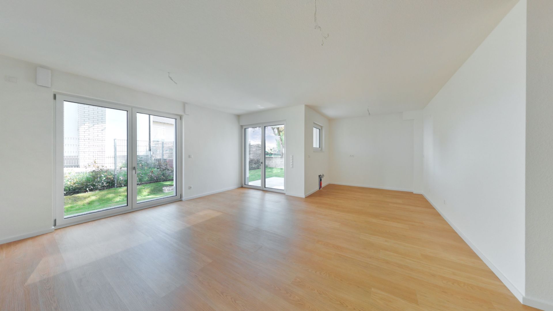 Helles, leeres Wohnzimmer mit großen Fenstern und Zugang zum Garten, Parkettboden.