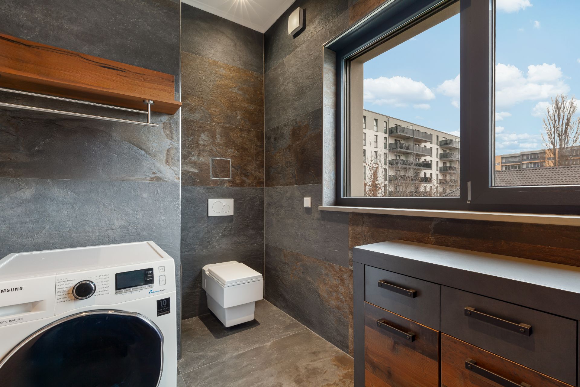 Modernes Bad mit Waschmaschine, Toilette und großem Fenster mit Blick nach draußen.