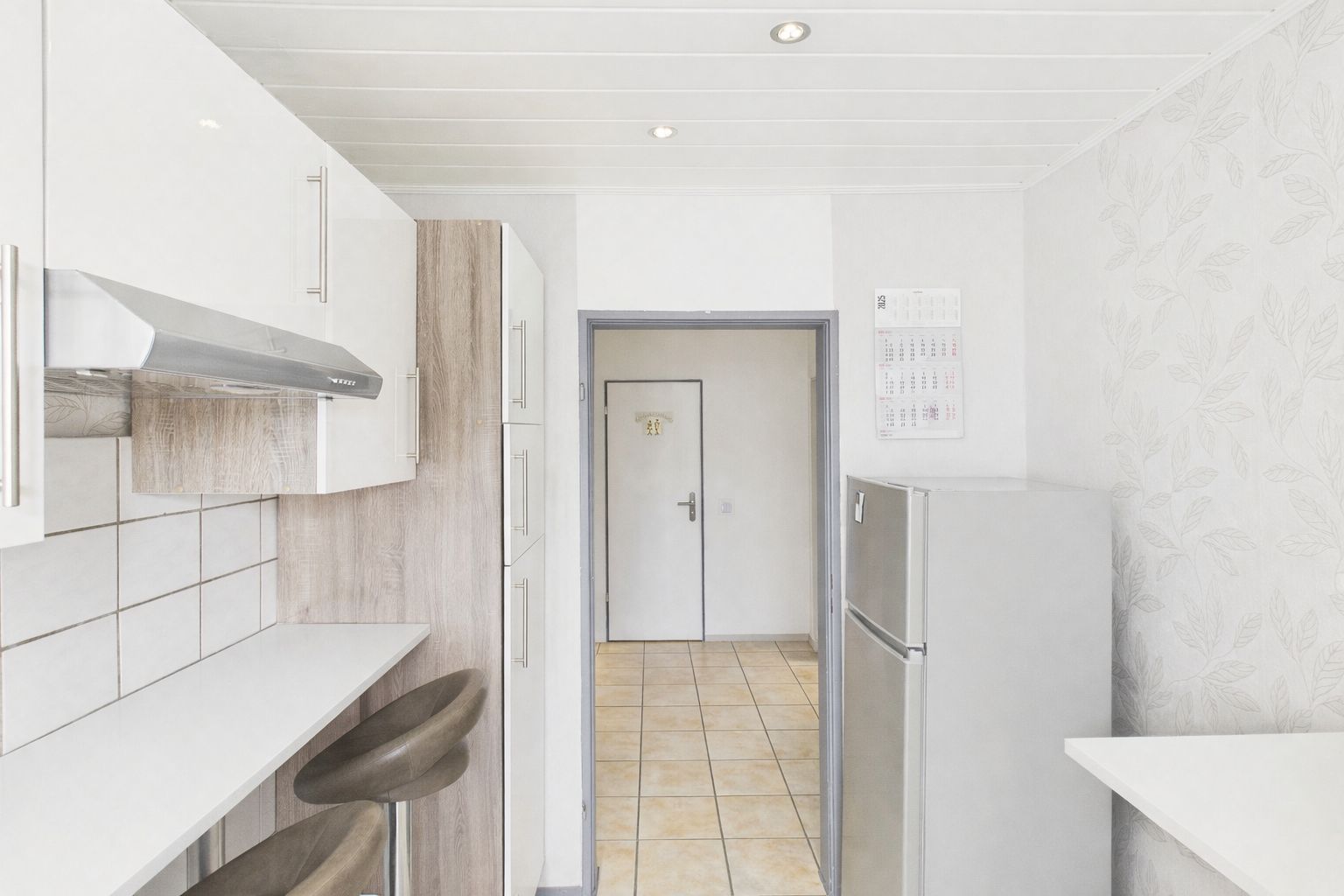 Helle Küche mit weißen Schränken, zwei Barhockern und einem silbernen Kühlschrank.