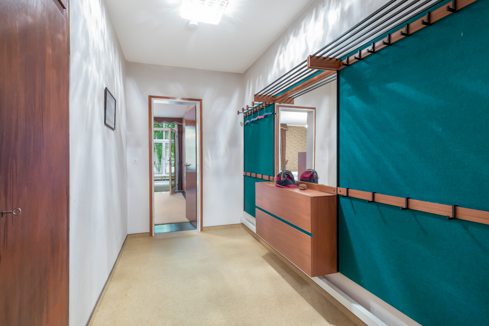 Flur mit Garderobe, Spiegel, Holzkommode und türkisfarbenen Wandpaneelen.
