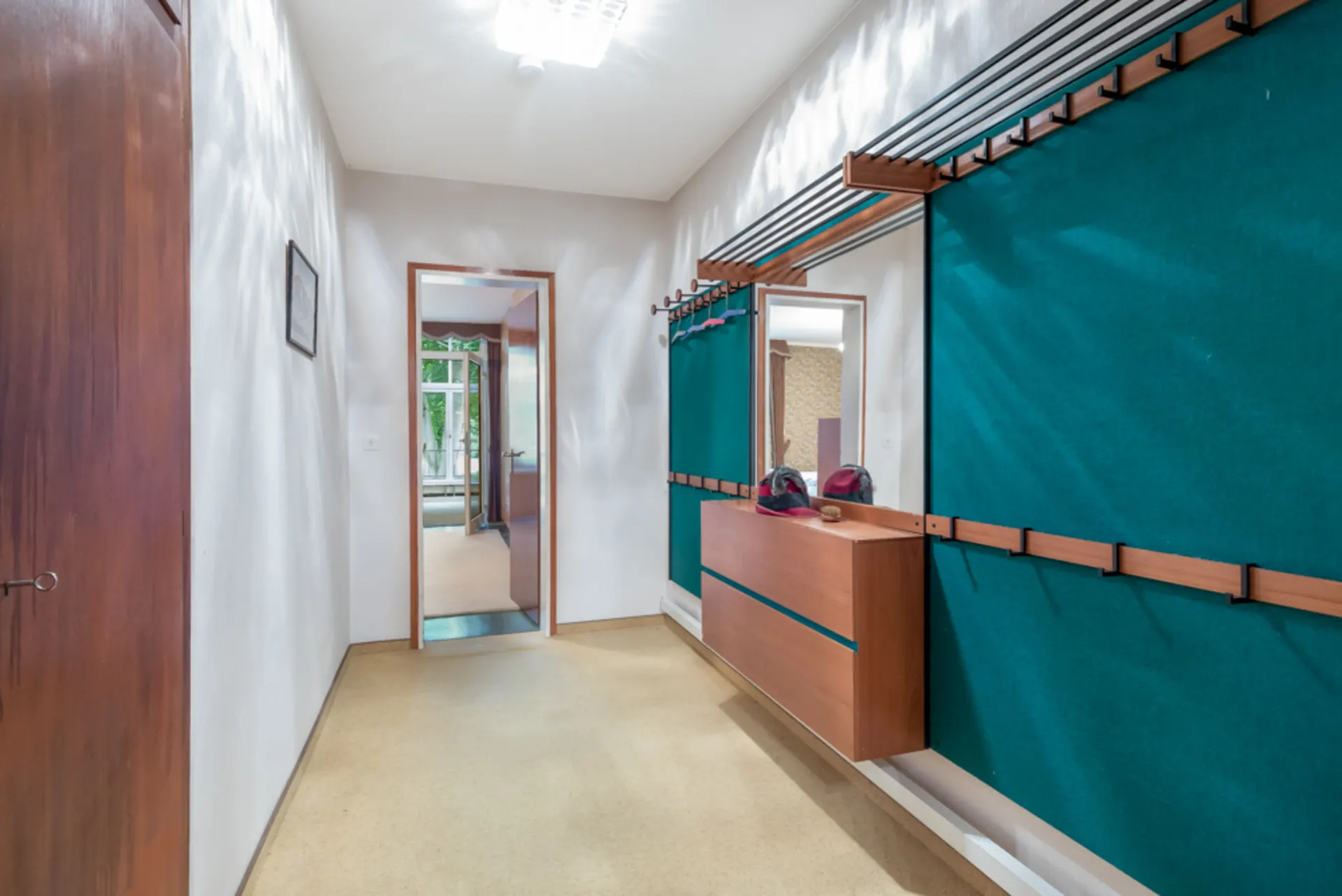 Flur mit Garderobe, Spiegel, Holzkommode und türkisfarbenen Wandpaneelen.