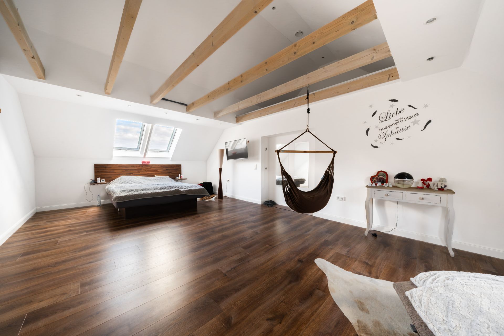 Großes Schlafzimmer mit Holzfußboden, Bett, Hängesessel und sichtbaren Holzbalken an der Decke.