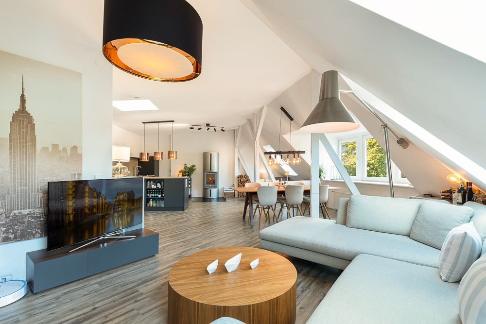 Modernes, helles Wohnzimmer mit Sofa, Rundtisch, Fernseher und Essbereich unter Dachschrägen.