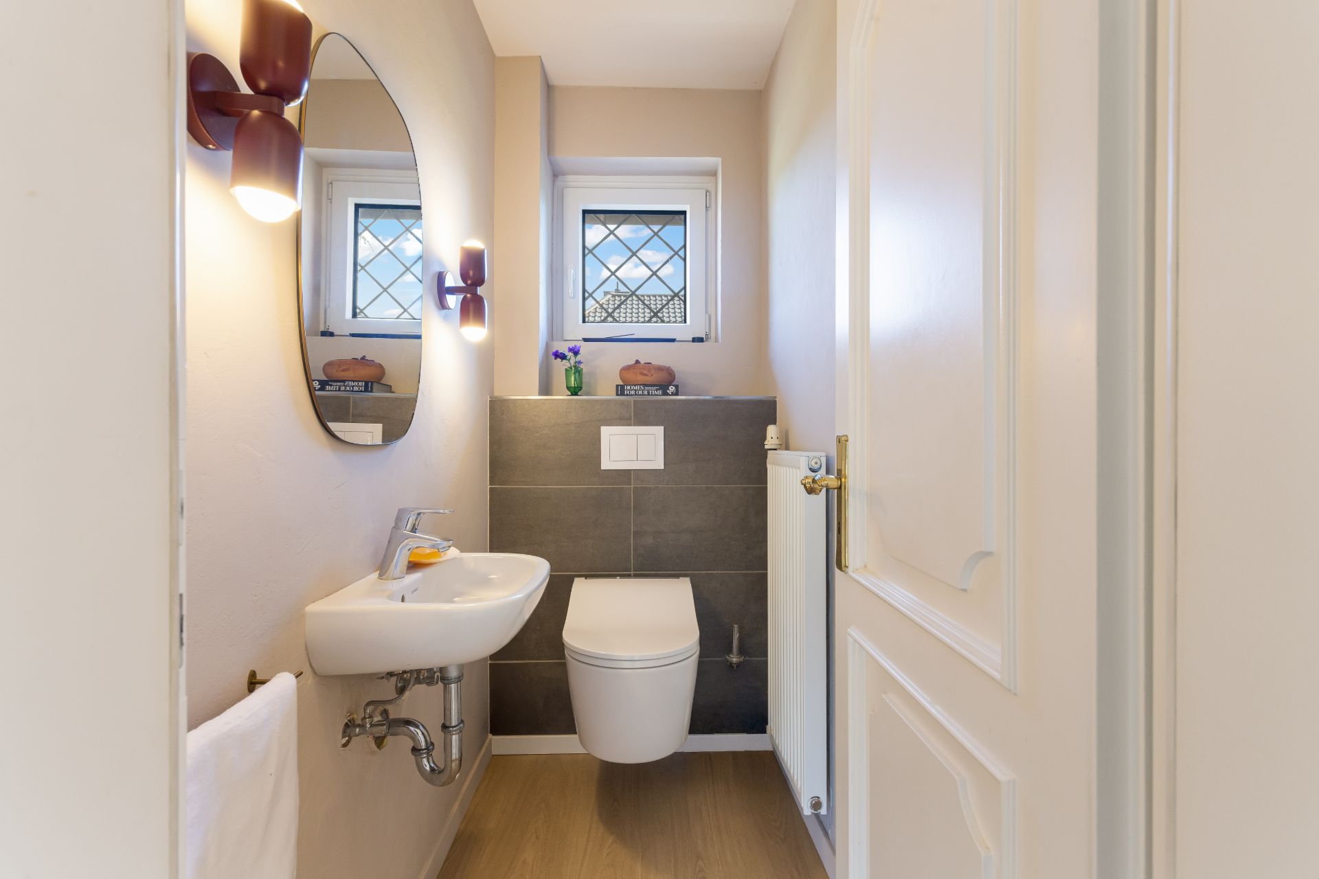 Kleines Badezimmer mit Wandtoilette, Waschbecken, Spiegel und Fenster.