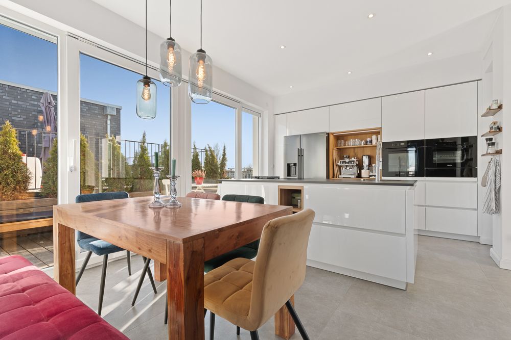 Moderne Küche mit Holztisch, bunten Stühlen und großen Fenstern zur Terrasse.