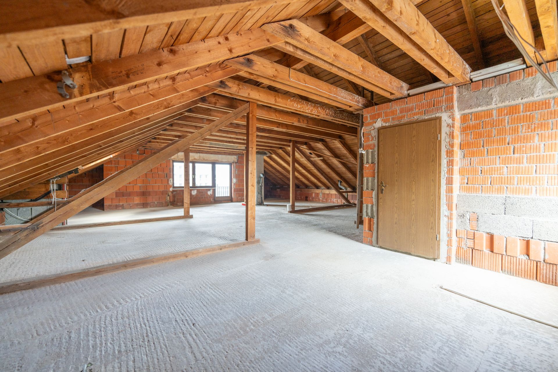 Geräumiger Dachboden mit Holzbalken, rohen Ziegelwänden und Fenster im Hintergrund.