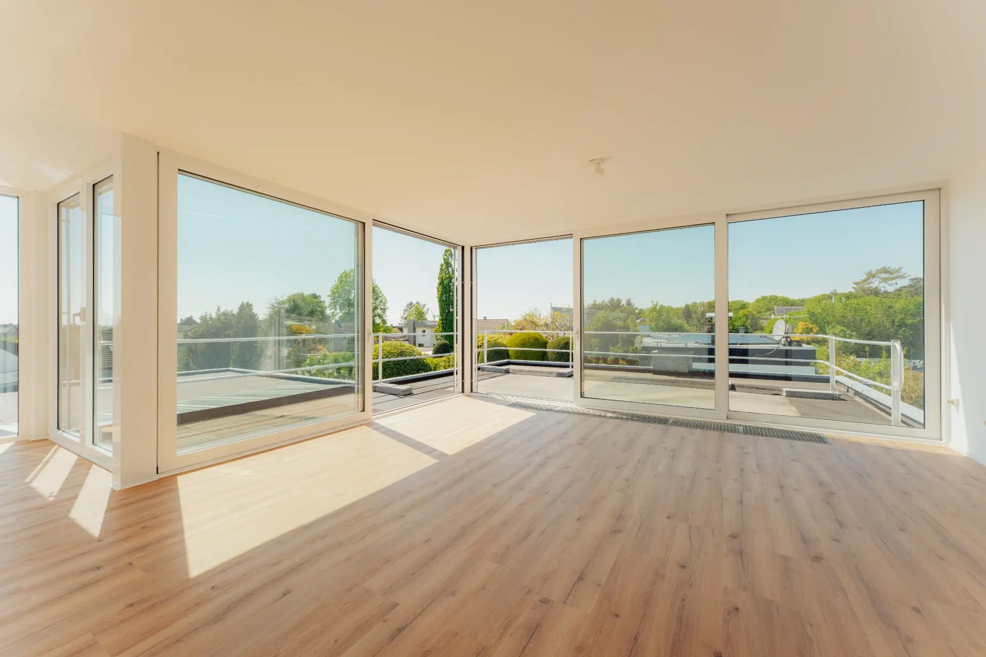 Helles Wohnzimmer mit großen Fenstern, Holzfußboden und Blick auf eine Terrasse.