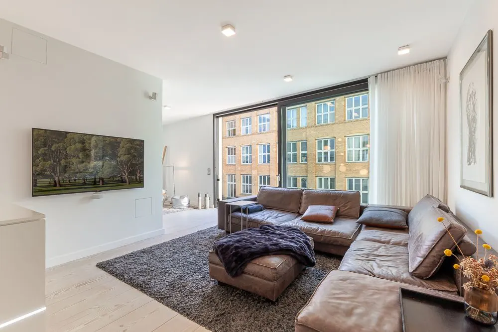 Modernes Wohnzimmer mit großer Eckcouch, Teppich, Wand-TV und bodentiefen Fenstern.