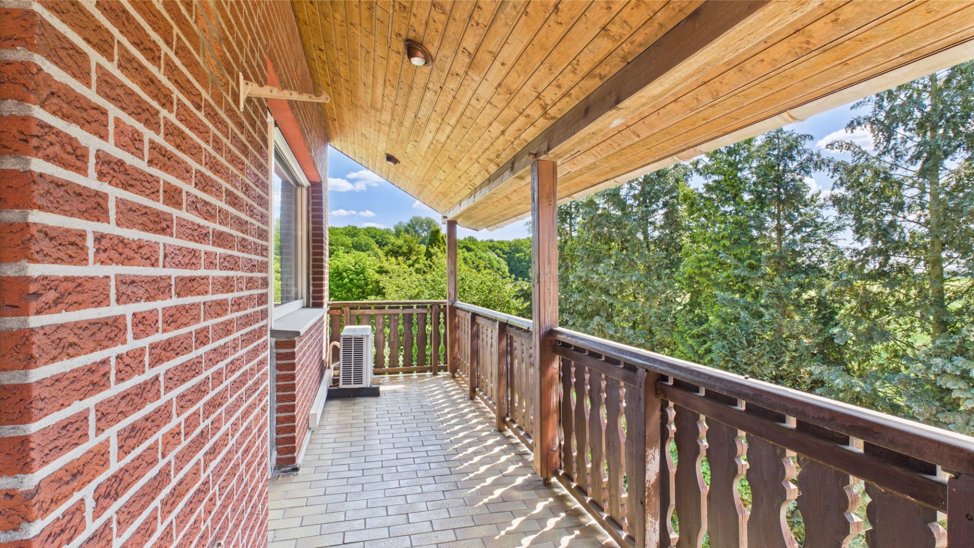 Überdachter Balkon mit Holzbalkon und Blick auf grüne Bäume.