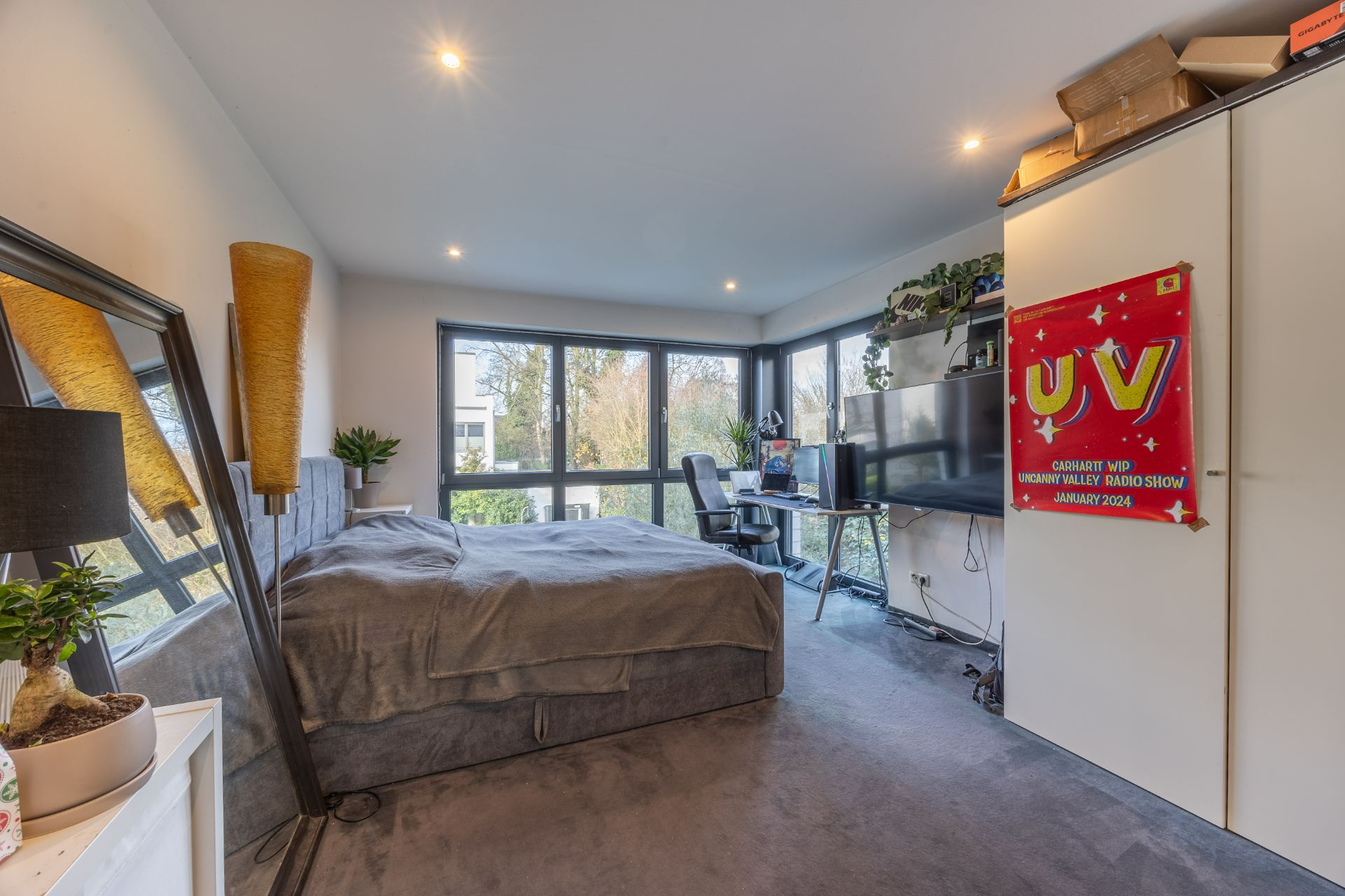 Helles Schlafzimmer mit Bett, Schreibtisch und großem Fenster mit Gartenblick.