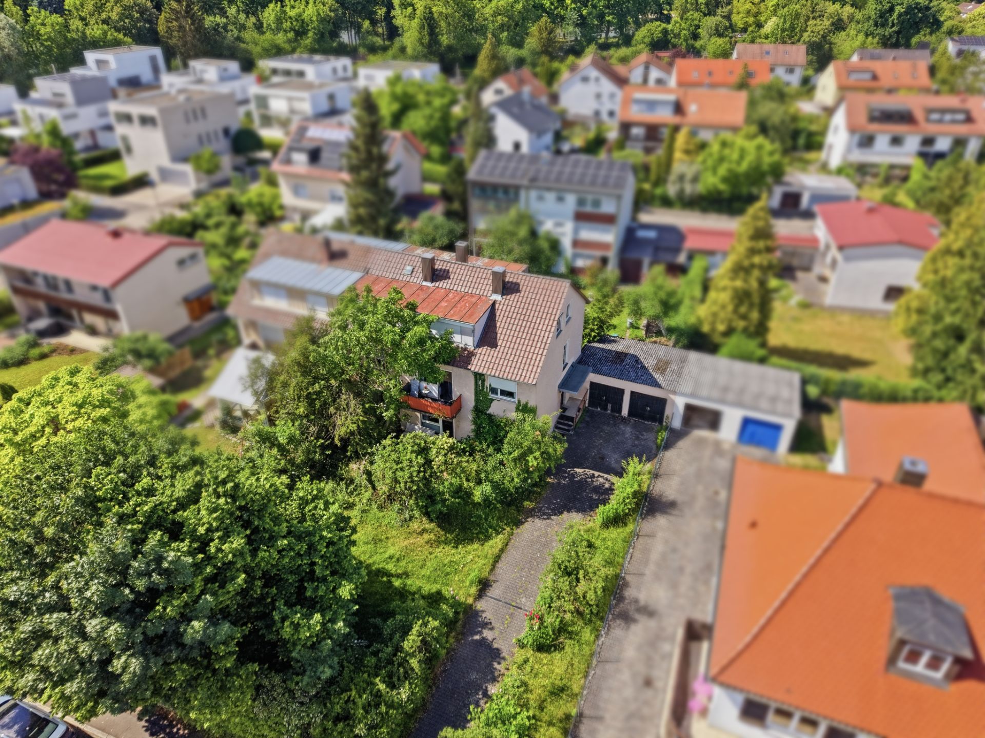 Luftaufnahme eines Wohnhauses mit Einfahrt und Garage, umgeben von weiteren Häusern und viel Grün.