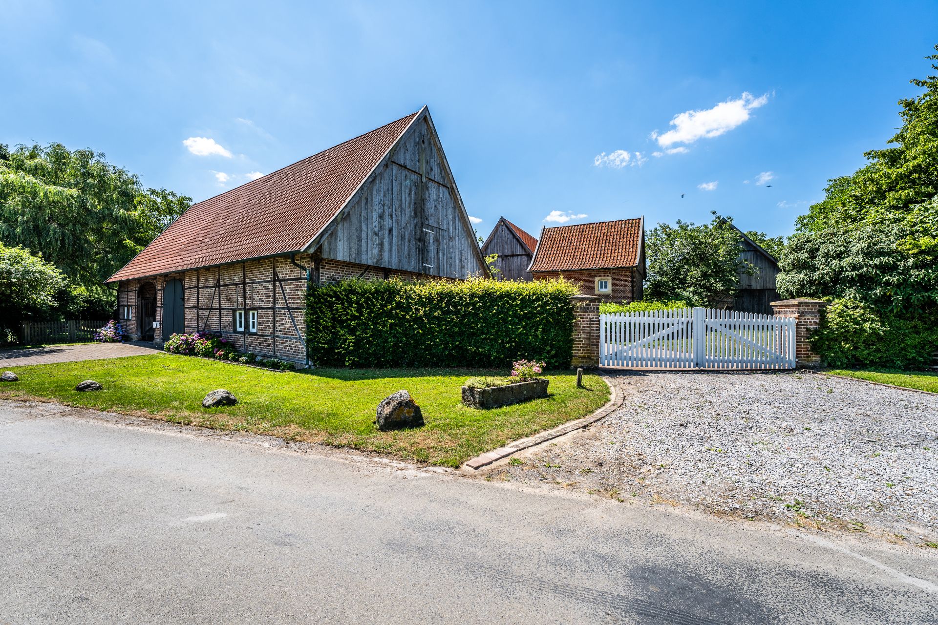Fachwerkhaus mit rotem Dach, Garten und weißem Holztor an Kieszufahrt.